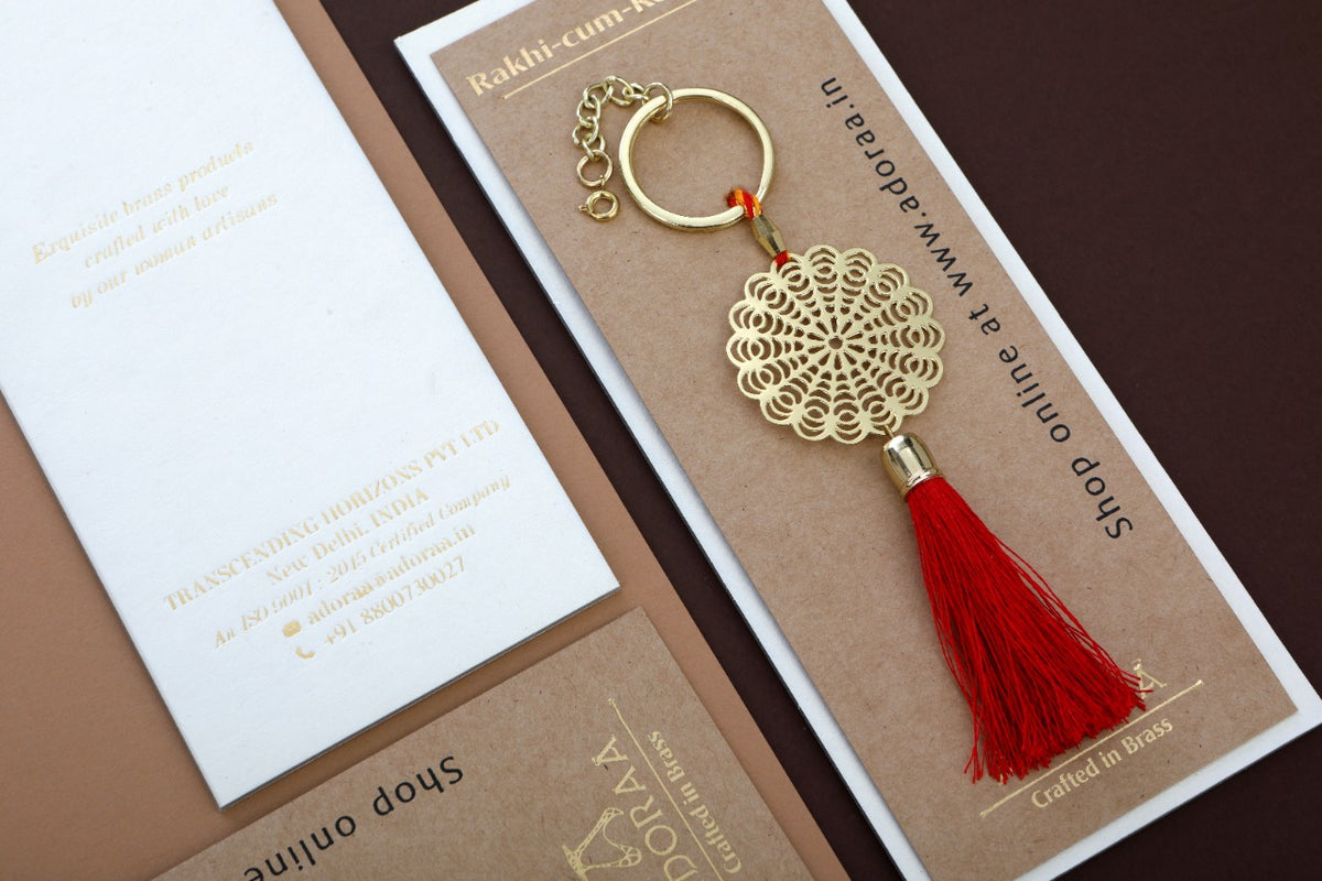 Floral design Rakhi for bhabhi with red hanging tassel cum keychain ring crafted in brass with golden finish